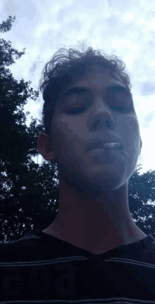 a young man is smoking a cigarette in front of trees