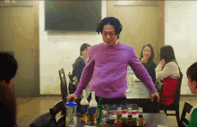 a man in a purple sweater is standing in front of a table