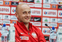 a man in a red jacket is sitting at a table in front of a microphone and smiling .