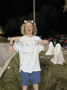 a boy wearing a white kanye t-shirt stands in front of ghosts