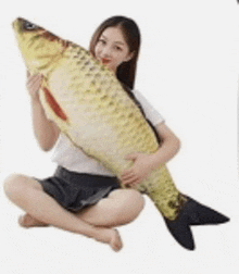 a woman is sitting on the floor holding a giant stuffed fish .