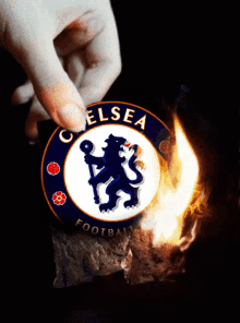 a hand is holding a chelsea football logo with flames coming out of it