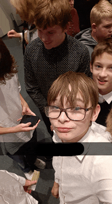 a boy wearing glasses is standing in a crowd of people