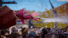 a person is holding an umbrella in front of a crowd of people while a pink flower is being sprayed with bubbles