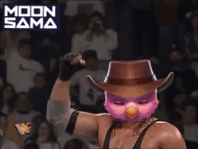 a wrestler wearing a cowboy hat and a pink bird mask flexes his arm