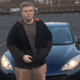 a young man stands in front of a blue car with a license plate that says ' tc ' on it