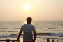 a man in a striped shirt stands on the beach at sunset