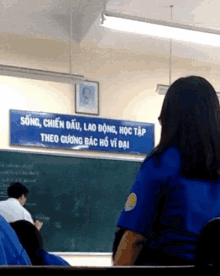 a woman sits in front of a chalkboard with a sign that says song chien dau lao dong hoc tap