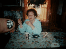 an elderly woman sitting at a table with a mug that says ' a ' on it