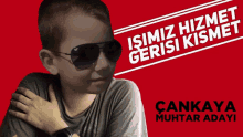 a boy wearing sunglasses stands in front of a red sign that says " isimiz hizmet gerisi kismet "