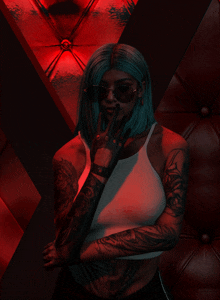 a woman with tattoos on her arms is wearing sunglasses and a white tank top