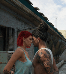 a man with dreadlocks and a woman with red hair look at each other in front of a building