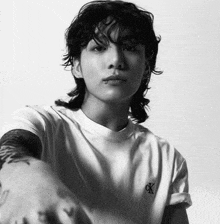 a black and white photo of a young man wearing a white t-shirt and a mullet .