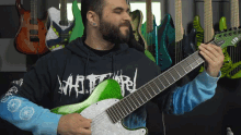 a man playing a guitar in front of a wall of guitars and a shirt that says ' metallica ' on it