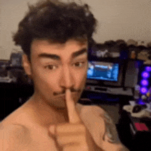 a shirtless man with a mustache is holding his finger to his mouth .