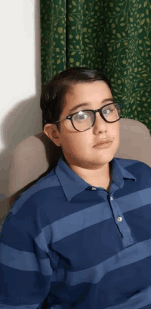 a young boy wearing glasses and a blue striped shirt is sitting on a chair .