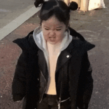 a little girl is making a funny face while wearing a black jacket .