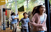 a group of children are running down a sidewalk in front of a building with clothes hanging on a clothesline .