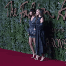 two women are standing on a red carpet in front of a wall that says " the fashion awards "