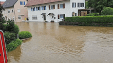 a flooded street with a house in the background and a red sign in the foreground