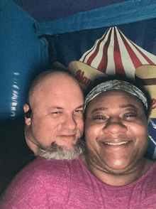 a man and a woman pose for a picture in front of a carnival tent