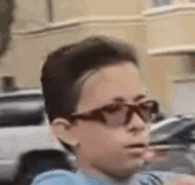 a young boy wearing glasses and a blue shirt is standing in front of a building .