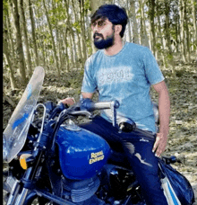 a man sitting on a blue royal enfield motorcycle in the woods