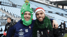 a man wearing a christmas tree hat and a man wearing a santa hat pose for a picture