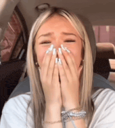 a blonde woman with white nails is covering her face with her hands