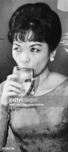 a black and white photo of a woman drinking a glass of water .