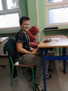 a boy sits at a desk in a classroom and smiles