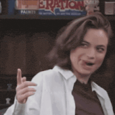 a woman in a white shirt is making a funny face in front of a shelf that says eraton