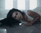 a woman in a white dress is laying on the floor looking at the camera