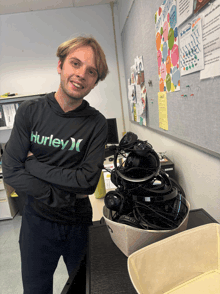 a man wearing a hurley hoodie stands in front of a pile of headphones