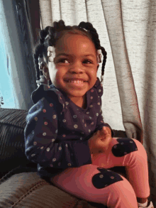 a little girl wearing polka dot pants and a blue sweatshirt smiles for the camera