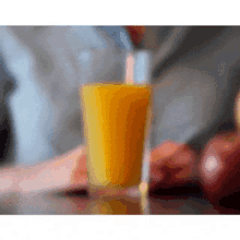 a glass of orange juice is sitting on a table with apples in the background .