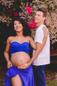 a pregnant woman in a blue dress stands next to a smiling man