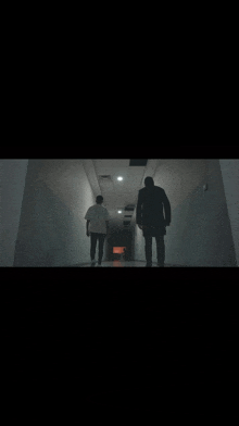 a man and a woman are walking down a dark hallway