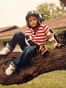 a young boy wearing a helmet and knee pads sitting on a tree branch