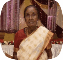 an elderly woman wearing a white saree and a red shirt is standing in a room .