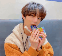 a young man is eating a candy bar while wearing a fur coat .