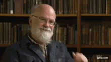 a man with a beard and glasses is sitting in front of a bookshelf in a library and smiling .