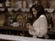 a woman in a white shirt is standing in front of a bar with bottles of alcohol on the shelf