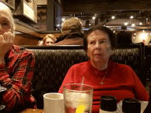 a woman in a red sweater sits at a table with a glass of water and salt and pepper shakers