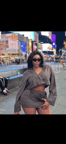 a woman wearing sunglasses and a crop top stands in front of a busy city street