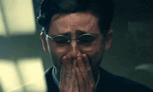 a man wearing glasses is crying with his hands over his mouth