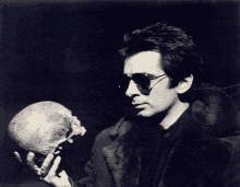 a man wearing sunglasses holds a skull in his hands