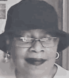 a woman is wearing a hat and glasses and smiling in a black and white photo .