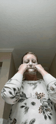 a woman wearing a floral sweater is applying a foam mask to her face