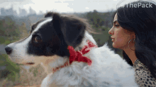 a black and white dog with a red bow around its neck is looking out a window next to a woman